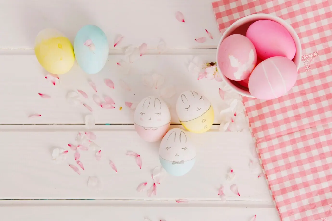 Ein Set aus Ostereiern zwischen Blütenblättern in der Nähe einer Serviette und einer Schüssel.