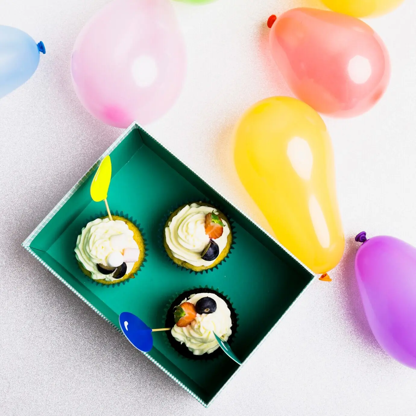 Kleine Cupcakes in einer grünen Box mit Luftballons